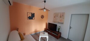 Uma sala de estar com sofá, televisão em um suporte, mesa pequena e obras de arte nas paredes.
