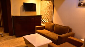 A cozy living room with a sofa, a coffee table, a TV mounted on the wall, and a curtain. - Hotel Cambean (Durg)