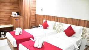 A hotel room with two beds, each with a red bedspread and white pillows. There is a wooden headboard with decorative patterns, a small wooden side table with a kettle and a magazine, and a red pillow on the right side of the bed. - Hotel Cambean (Durg)