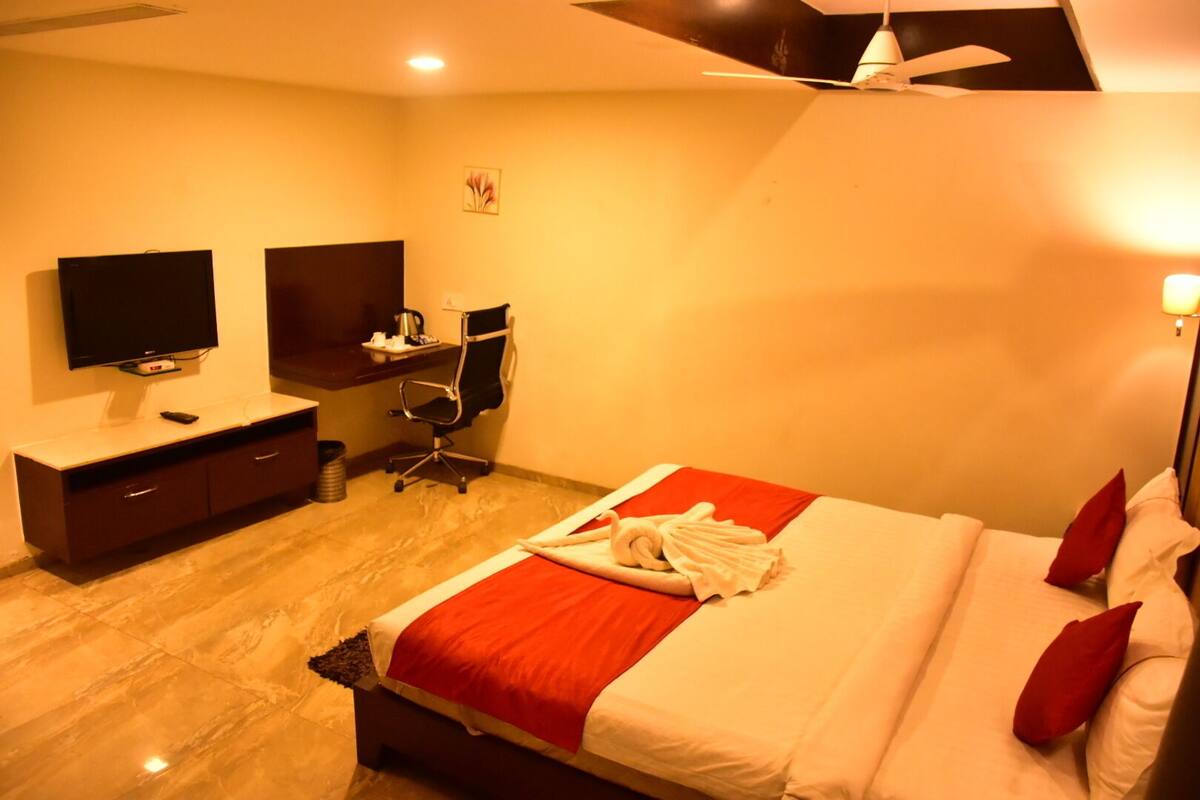 A hotel room with a bed, a desk, a chair, a television, and a ceiling fan.