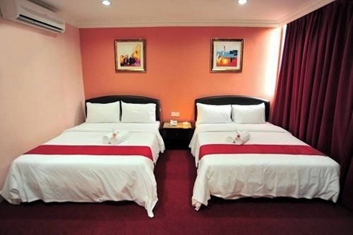 Quarto de hotel com duas camas, um tapete vermelho e dois quadros na parede.