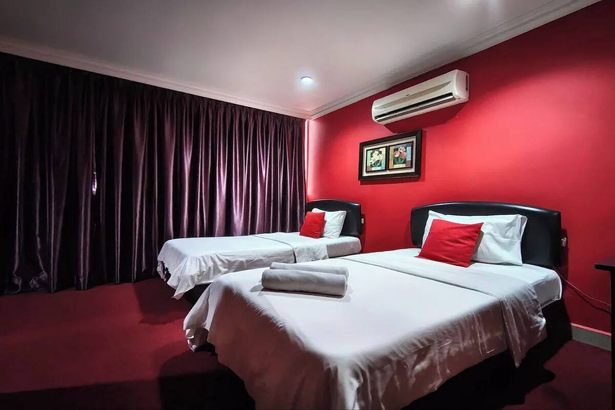 Quarto de hotel com duas camas, paredes vermelhas, ar condicionado e uma luminária no teto.