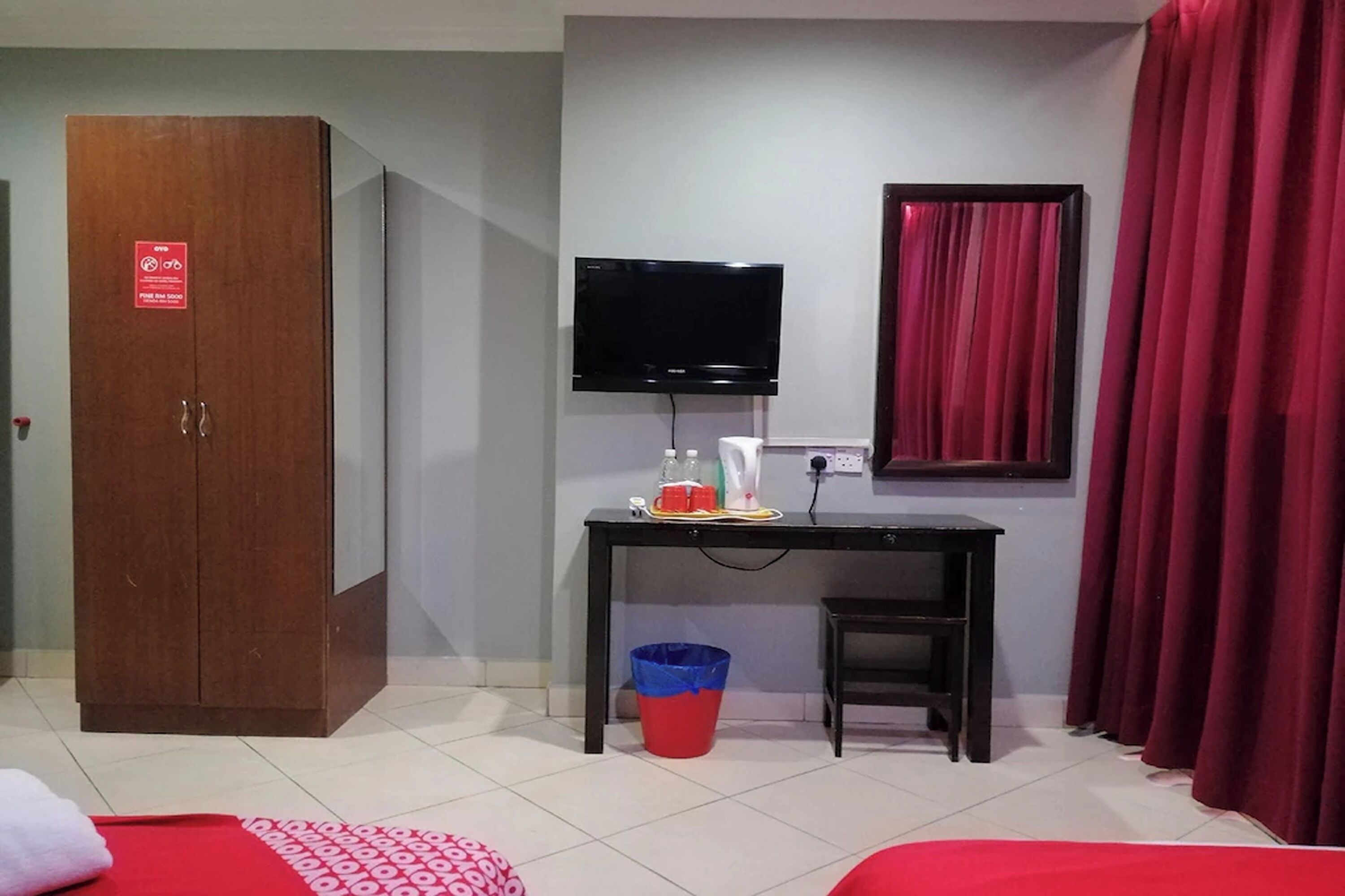 Una habitación con un armario de madera, un escritorio con televisor, una cortina roja y un cesto de basura.