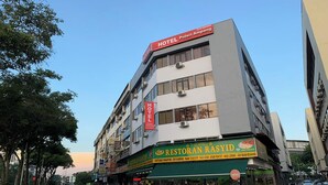 Un edificio de varios pisos con un cartel que dice 'HOTEL Puteri Ampang', un restaurante llamado 'RESTORAN RASYID' en la planta baja, y coches aparcados a lo largo de la calle.