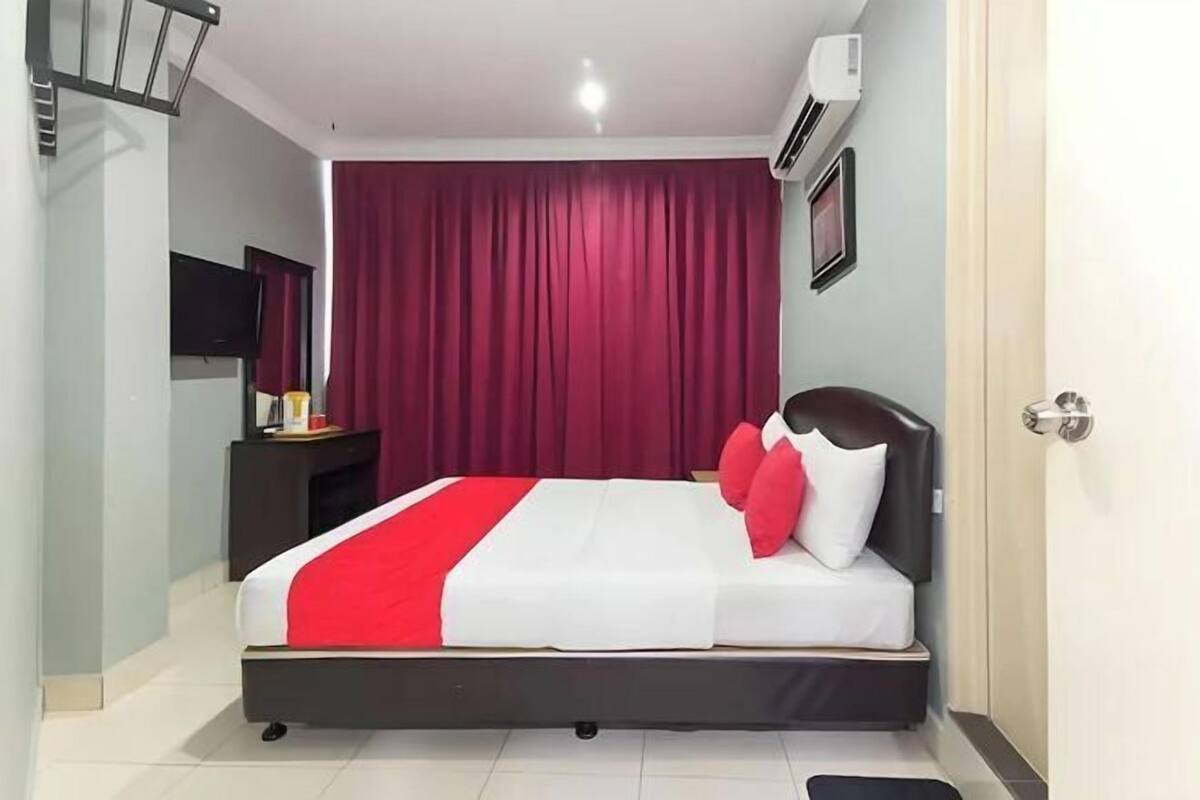 Quarto com cama, mesa de cabeceira, televisão e cortina vermelha.