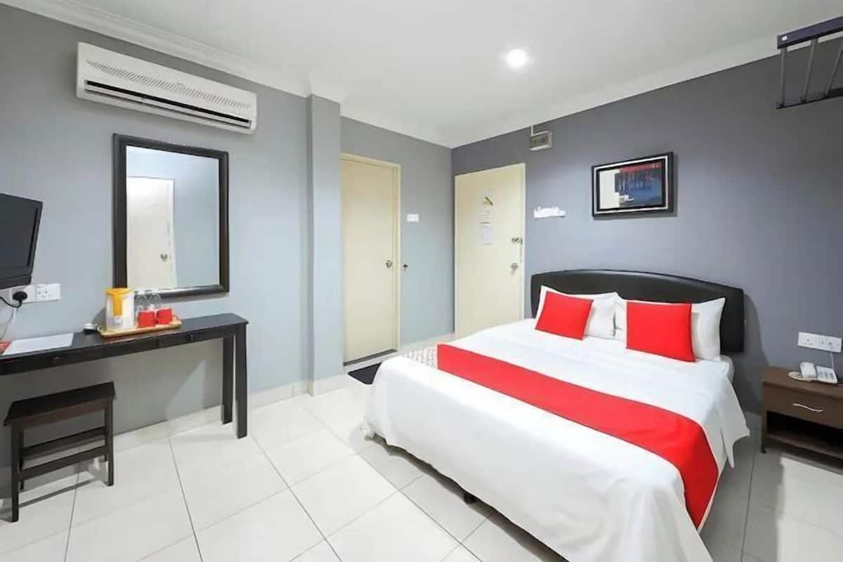 Habitación de hotel con cama, escritorio, silla, aire acondicionado, puerta y televisor montado en la pared.