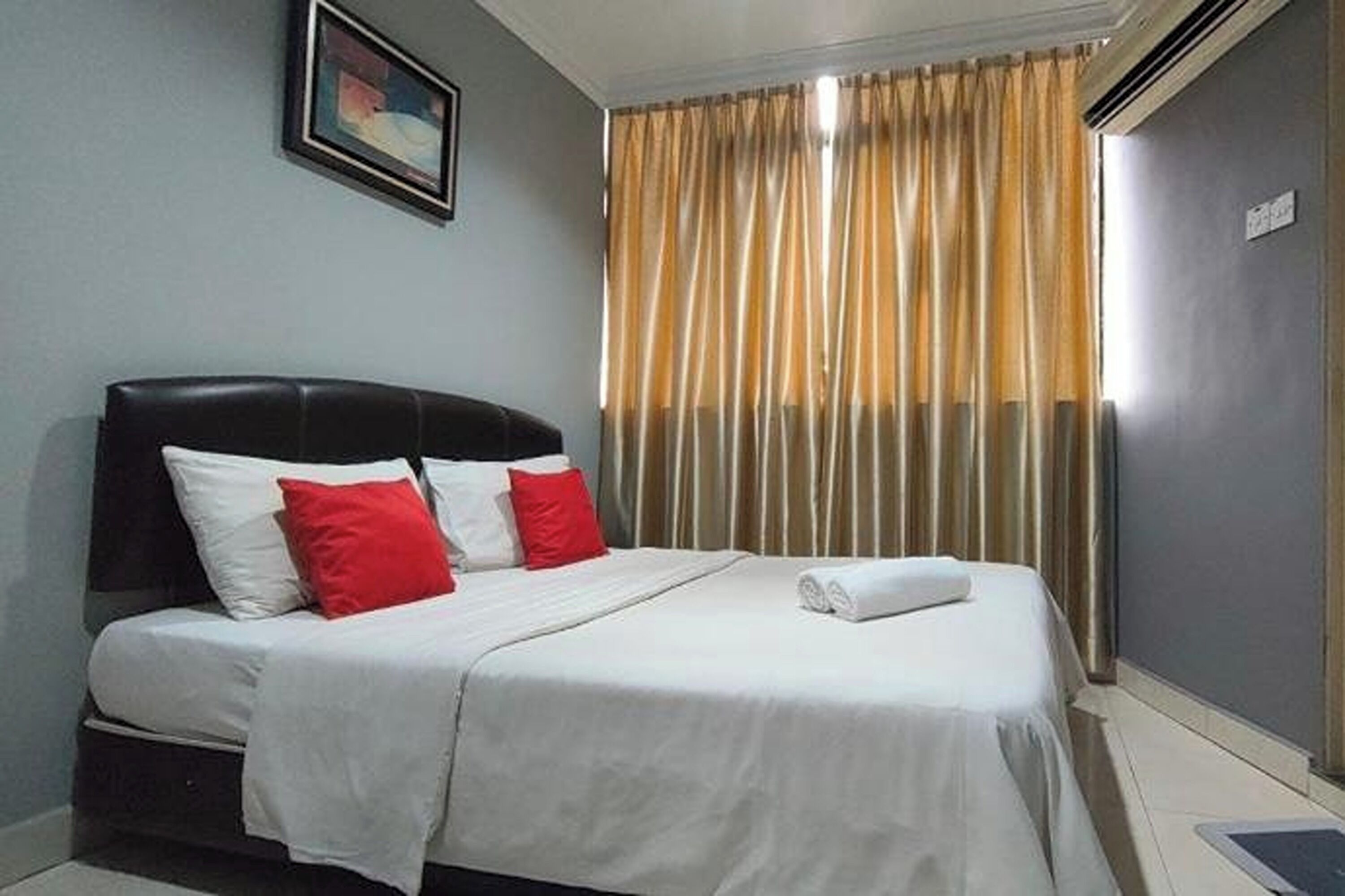 A hotel room with a bed, a headboard, a window with curtains, and a wall-mounted picture.