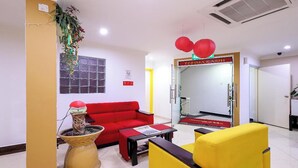 Un área de recepción con un sofá rojo, un sillón amarillo, una mesita y una planta decorativa.