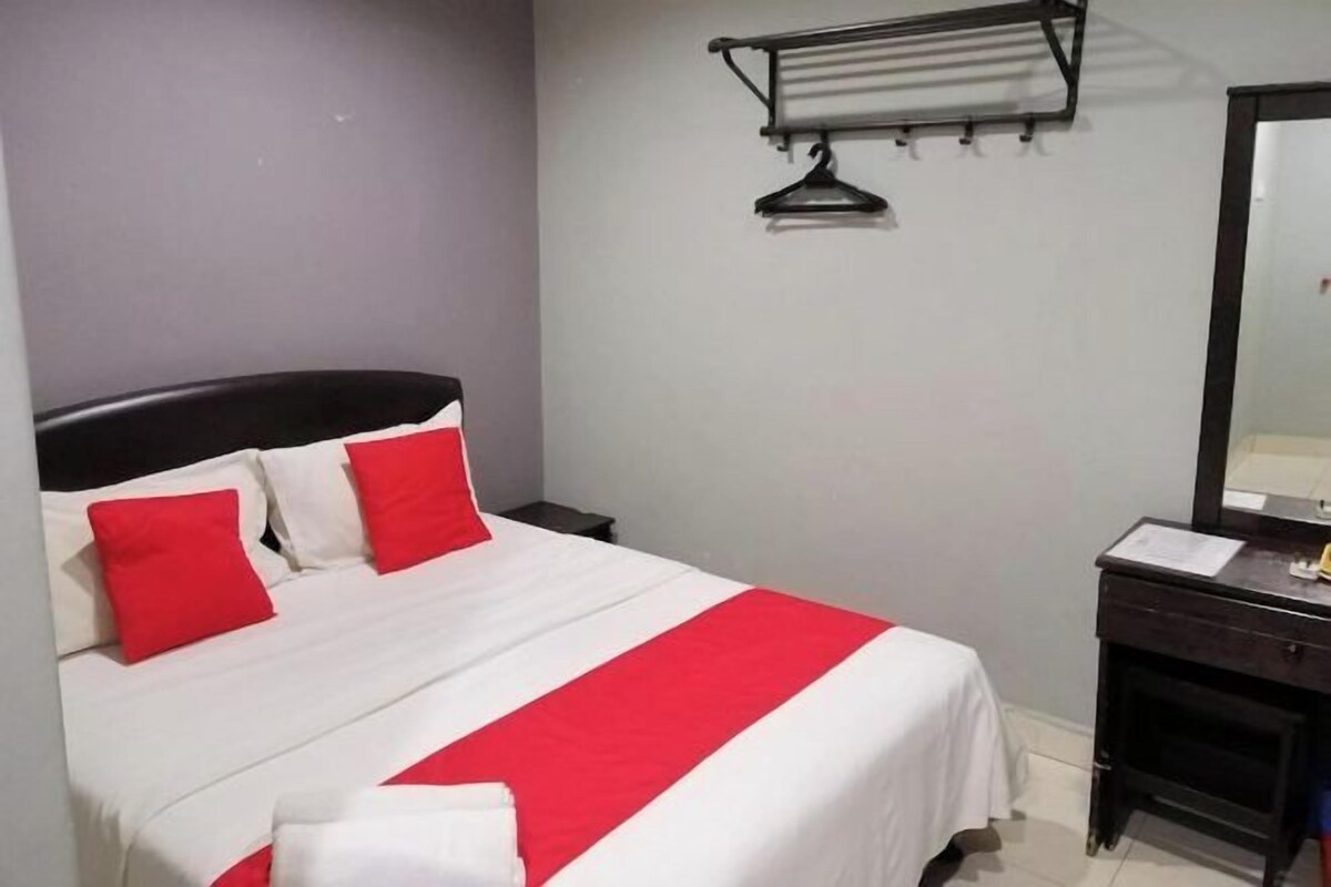Una cama con ropa de cama blanca y roja, una mesita de noche de madera oscura, un espejo y una toalla sobre la cama.