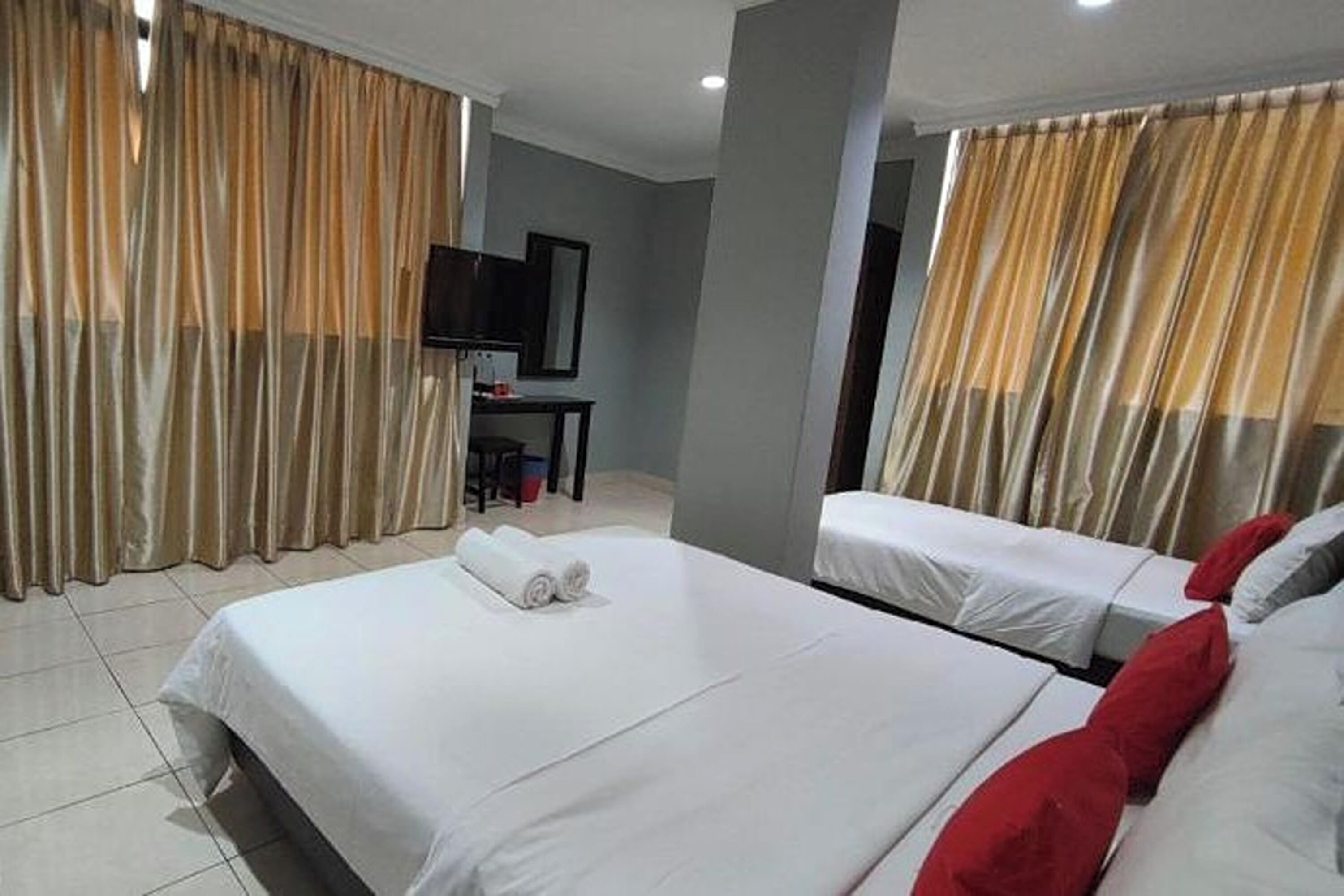 A hotel room with two beds, a desk with a TV, and curtains.