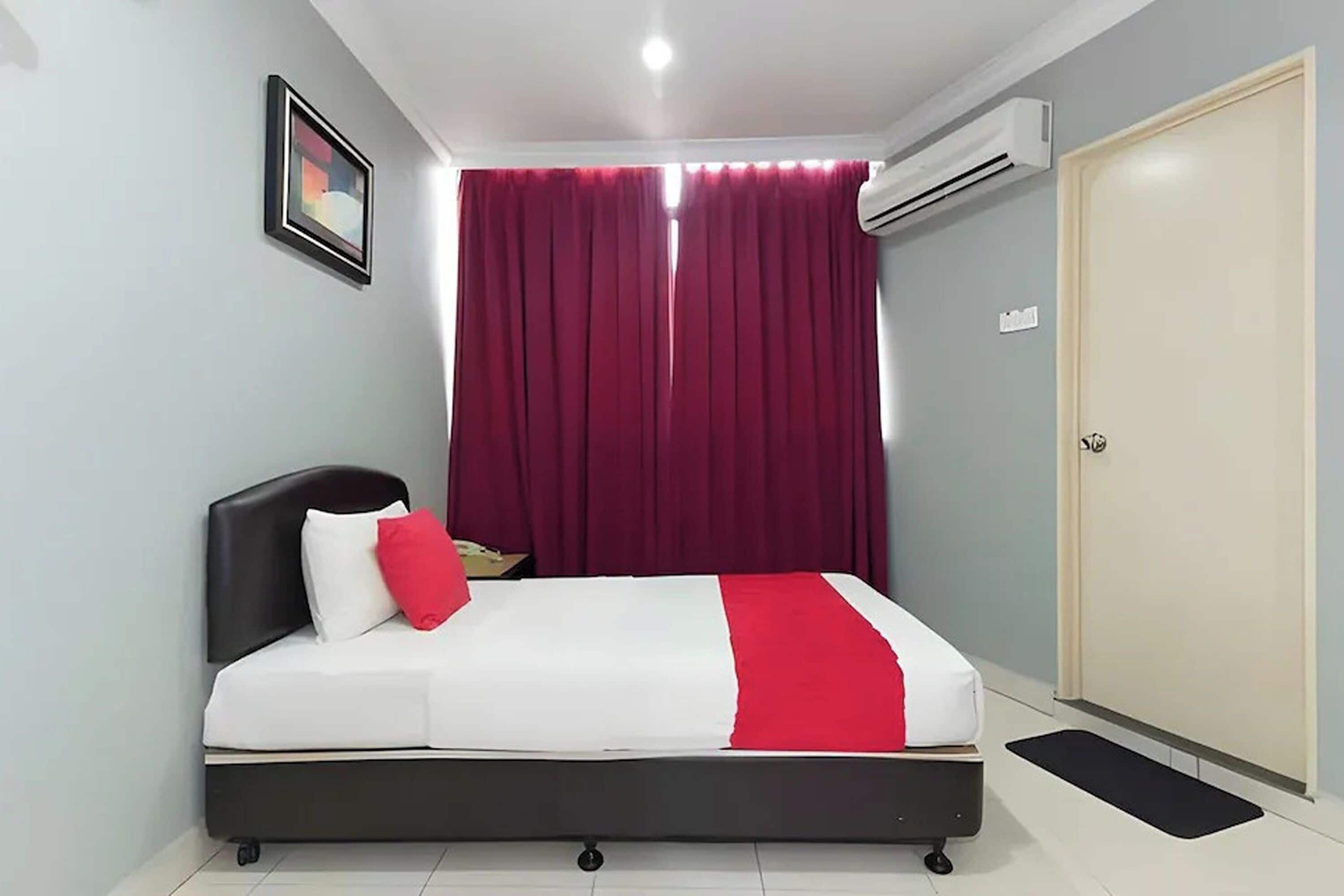 Un dormitorio con cama, puerta, equipo de aire acondicionado, un cuadro en la pared y ventana con cortinas.