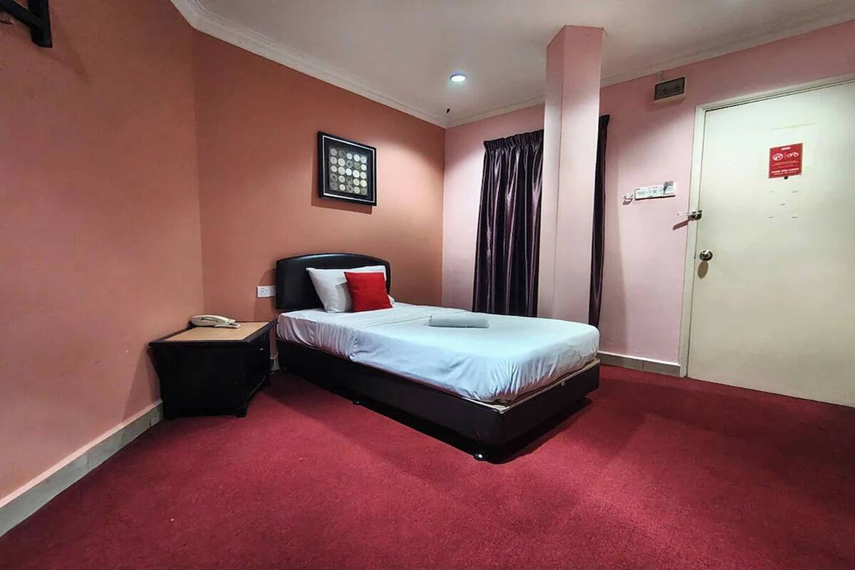 Quarto de hotel com uma cama, uma mesa com telefone, uma porta com placa e um quadro na parede.