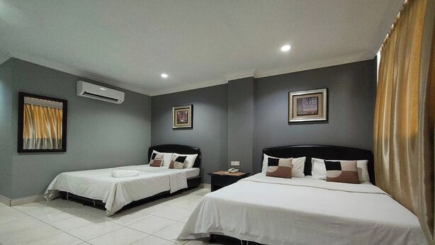 Habitación de hotel con dos camas individuales, una cama grande, una mesita de noche con un teléfono y un equipo de aire acondicionado en la pared.