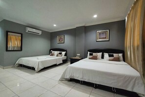 Quarto de hotel com duas camas de solteiro, uma cama grande, uma mesa de cabeceira com telefone e um aparelho de ar condicionado na parede.