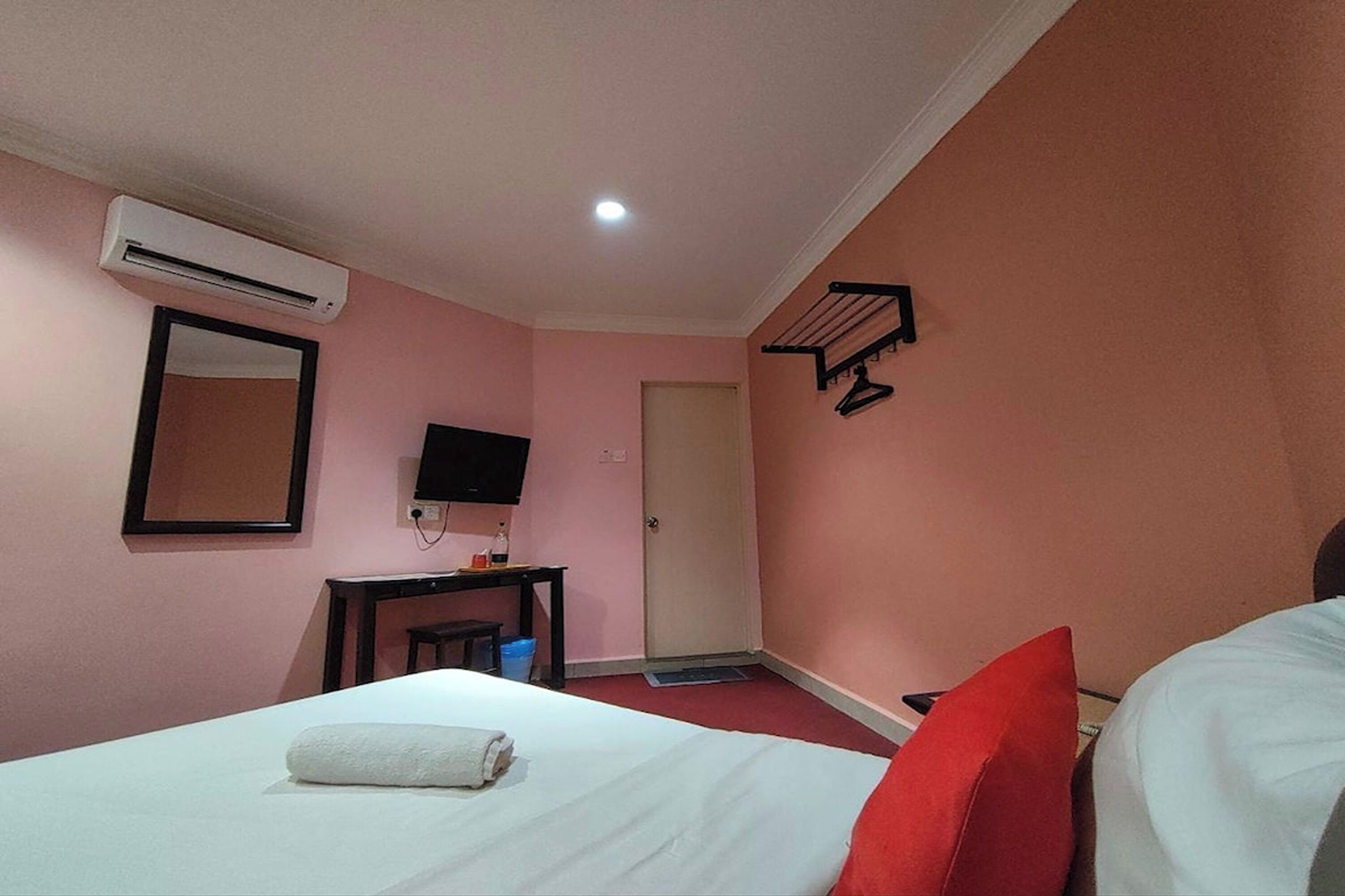 A hotel room with a bed, a TV, an air conditioning unit, a desk, and a door.
