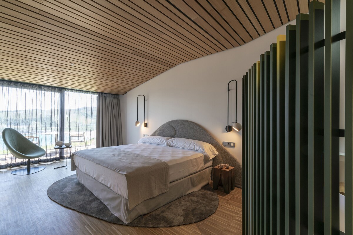 Un dormitorio moderno con una cama grande, techo curvo y vistas al exterior.