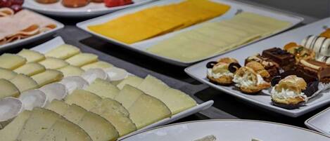 A buffet with various cheeses, fruits, and pastries.