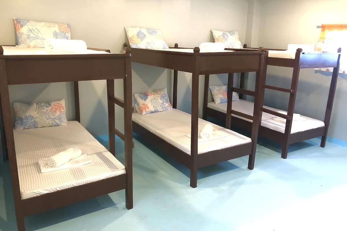 Four bunk beds with floral-patterned pillows and rolled towels, arranged in a row against a light blue wall.