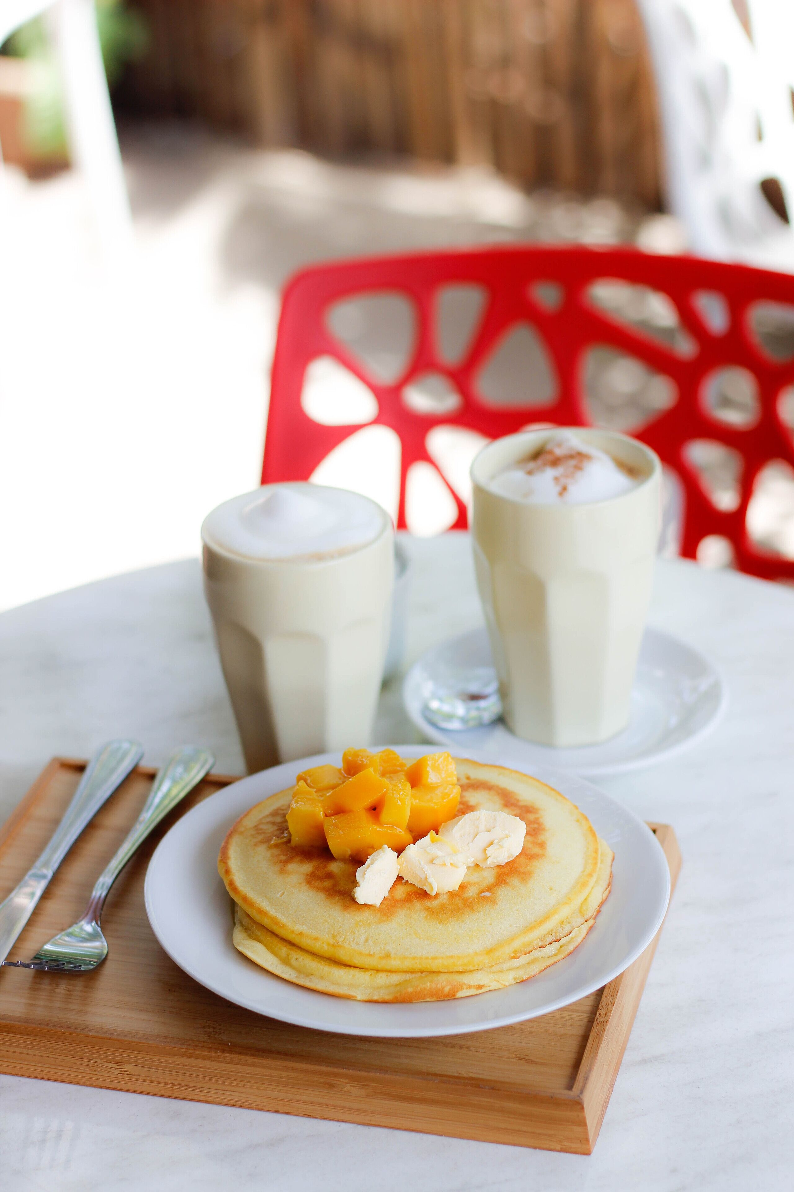 A breakfast setting with pancakes, fruit, and two milkshakes on a table.