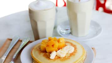 A breakfast setting with pancakes, fruit, and two milkshakes on a table.