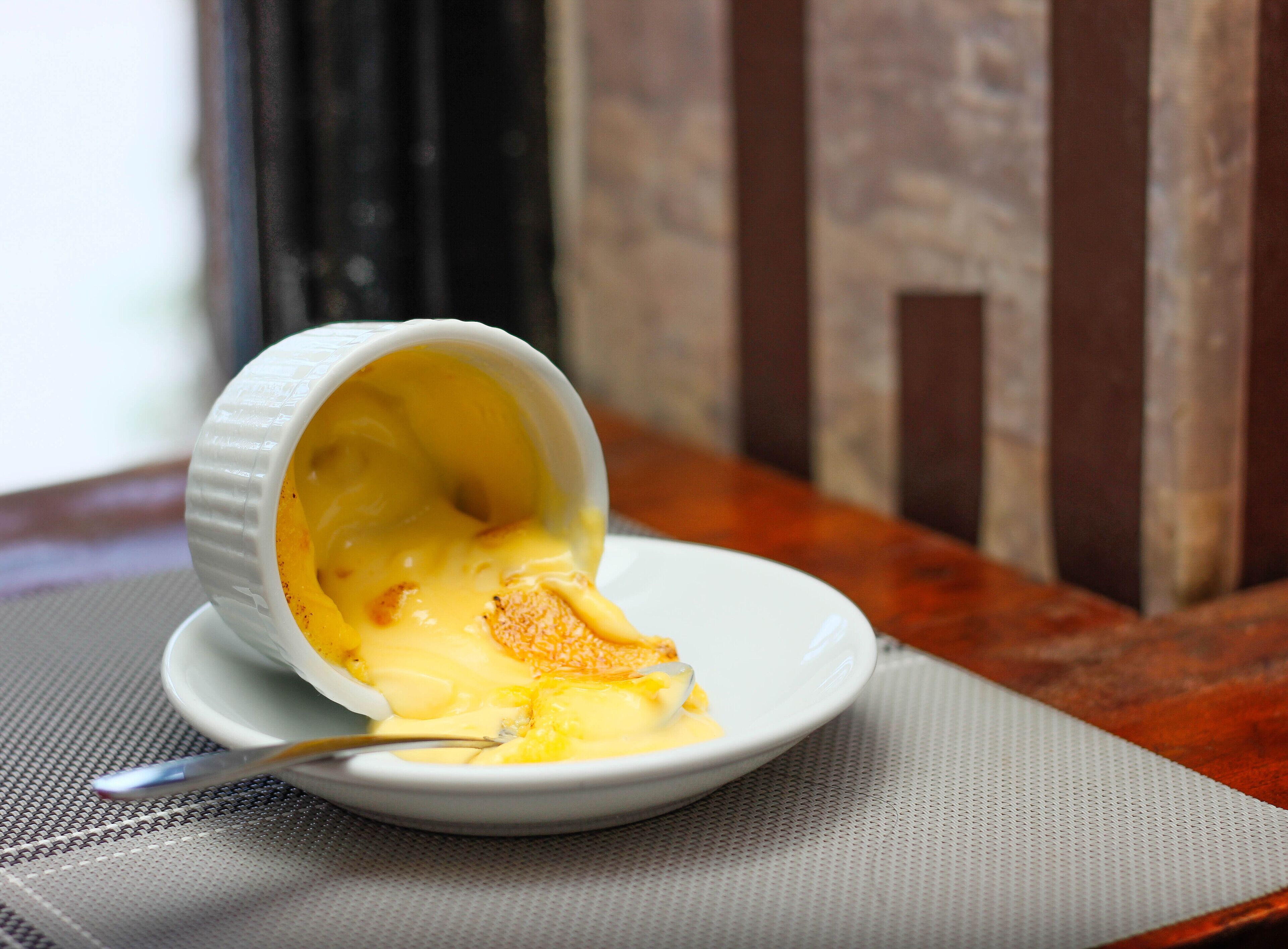 A dessert in a white ramekin on a white plate, with a spoon beside it.