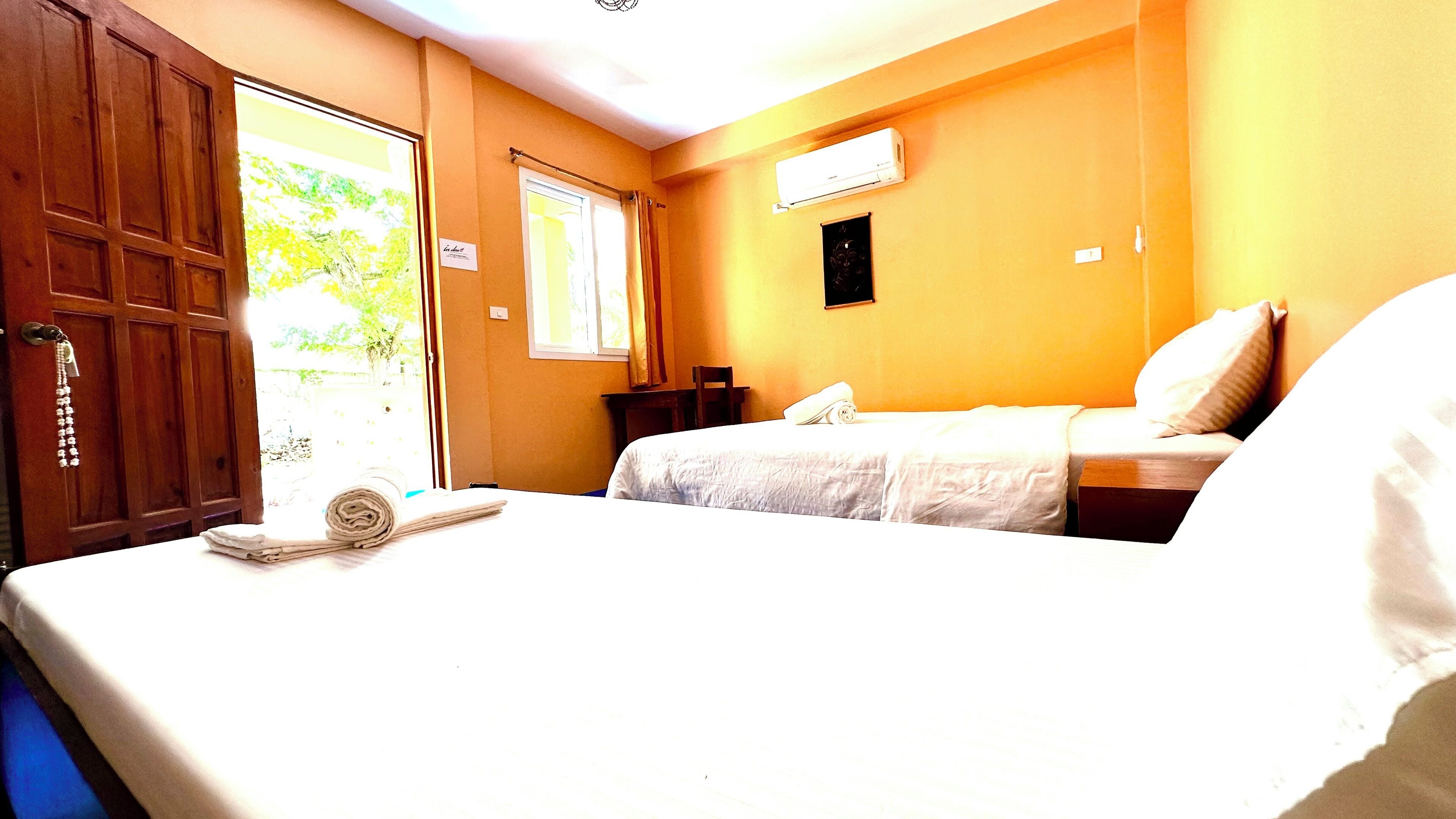 A hotel room with two beds, a wooden door, a window with curtains, and an air conditioning unit on the wall.
