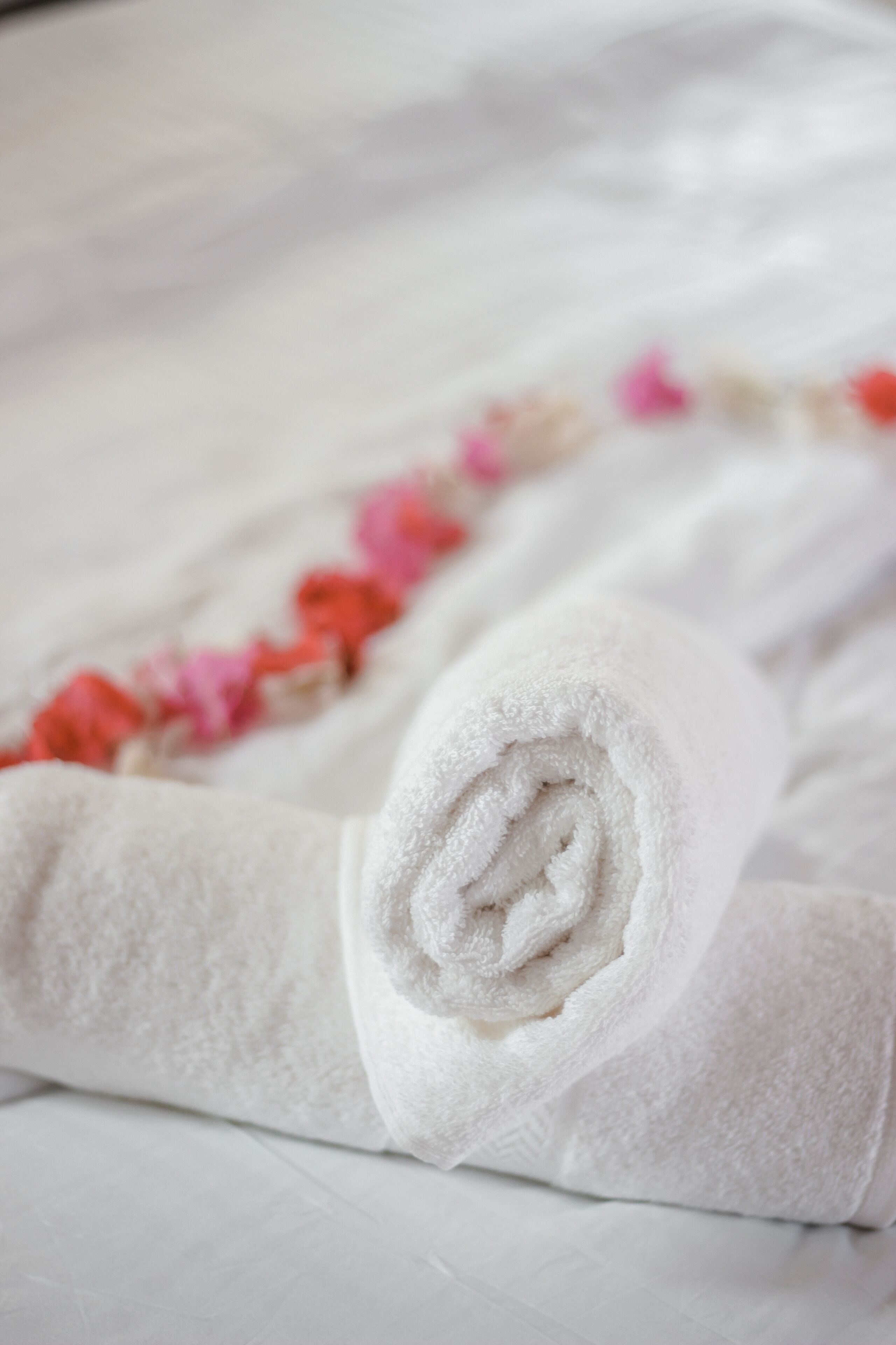 A neatly folded white towel with a rolled edge, placed on a white surface with a floral pattern.