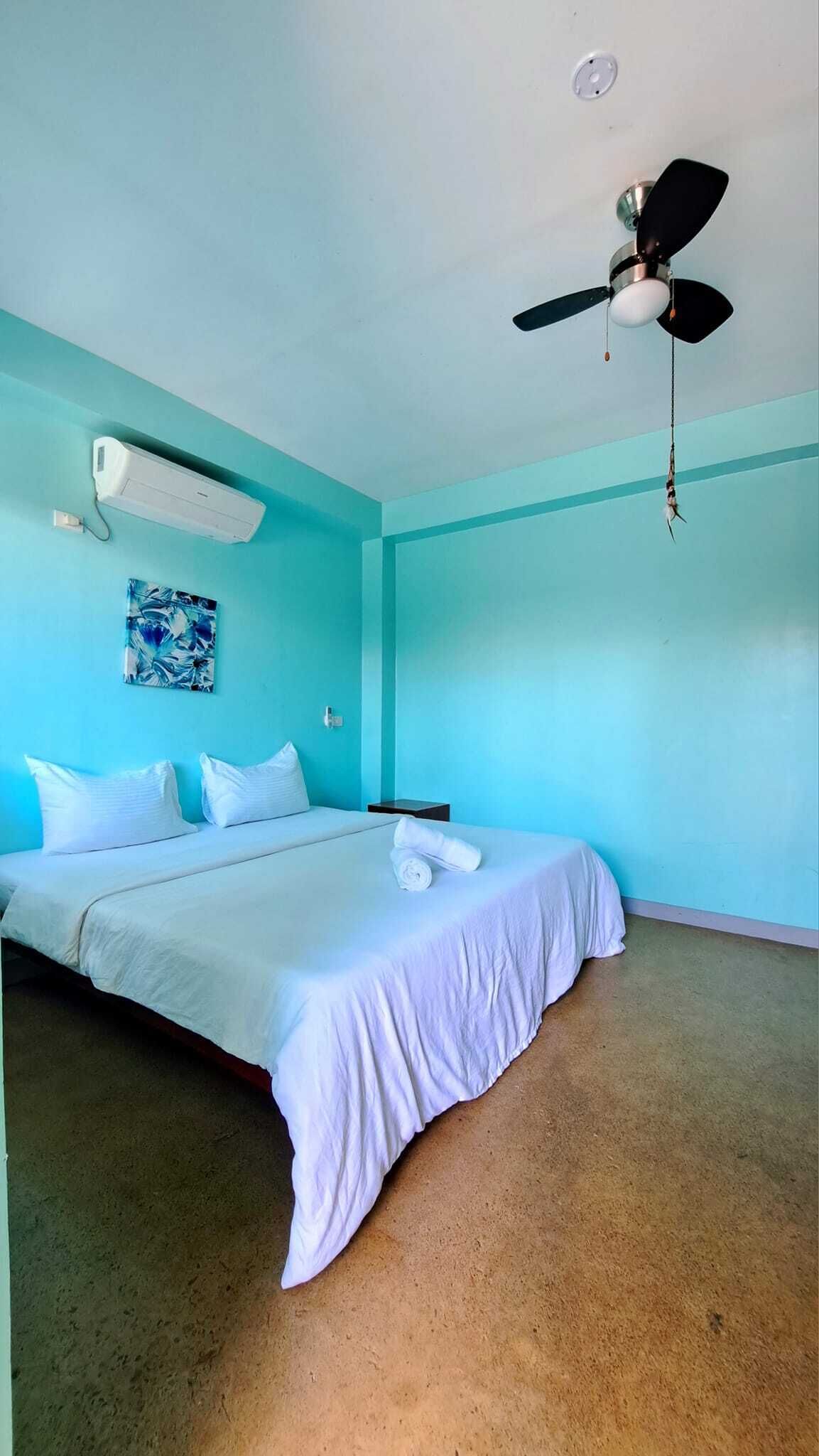 A bedroom with a bed, a ceiling fan, a wall-mounted air conditioner, and a painting.