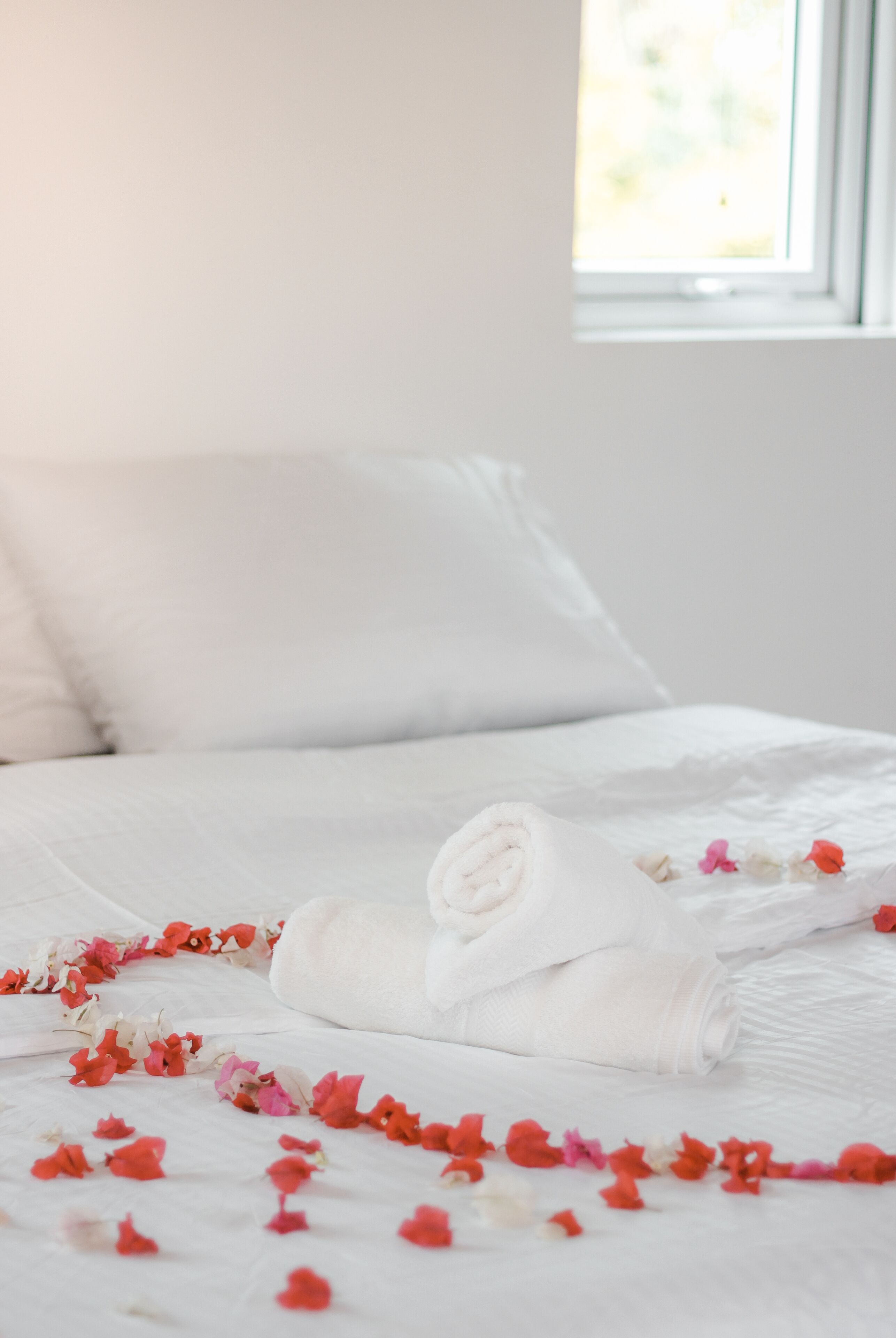 Una cama bien hecha con una toalla blanca enrollada y pétalos de flores esparcidos.
