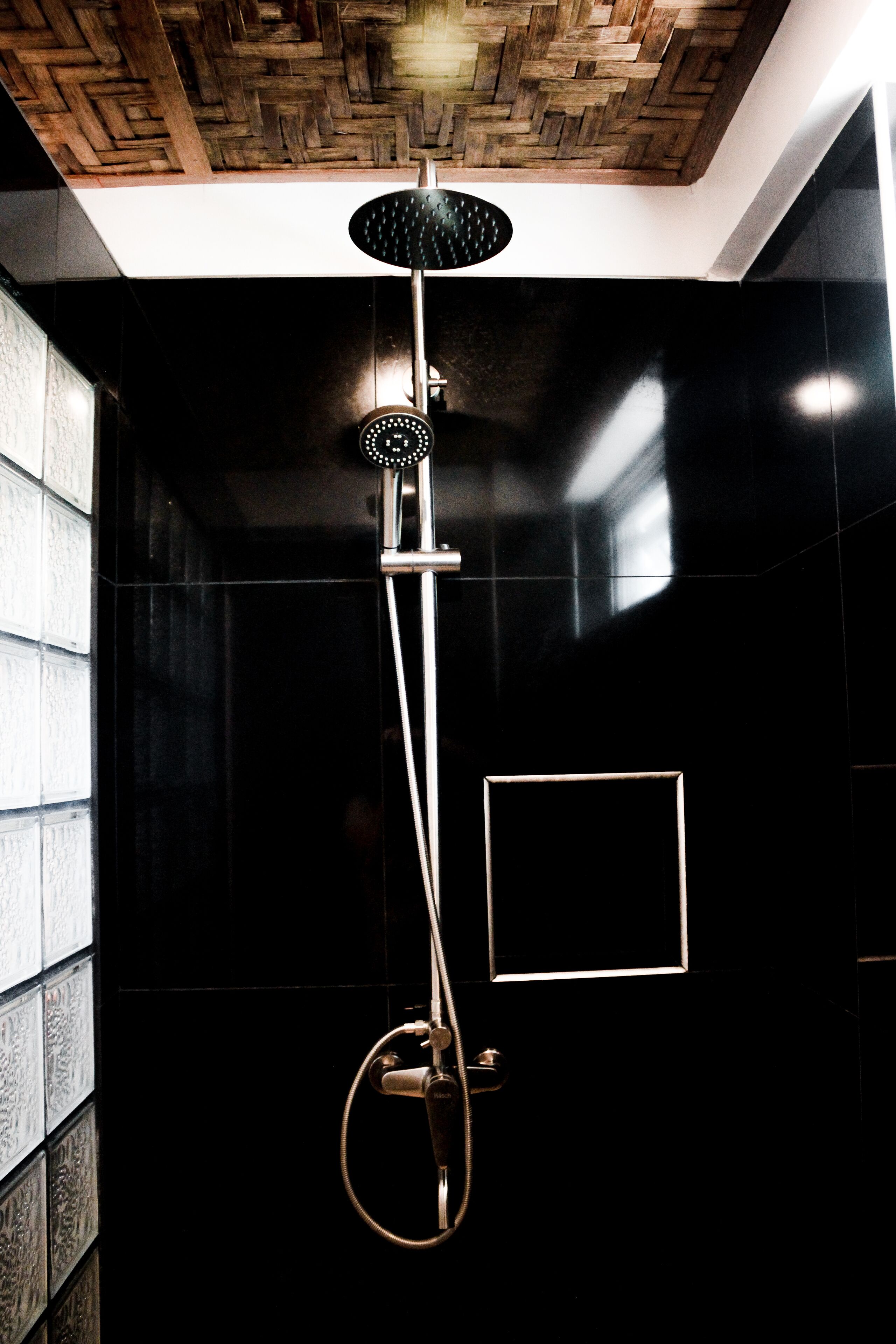 Een moderne douche met een houten plafond, zwarte wanden en een zichtbare douchekop.