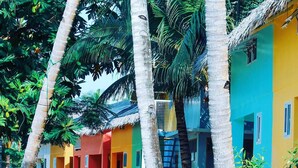 A row of colorful houses with a thatched roof, surrounded by lush greenery and palm trees. - Indai Aquasports and Resort (Santa Fe)