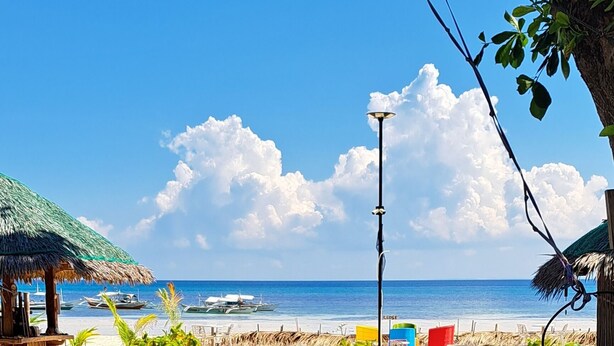 A beach with colorful chairs and a thatched-roof structure. - Indai Aquasports and Resort (Santa Fe)