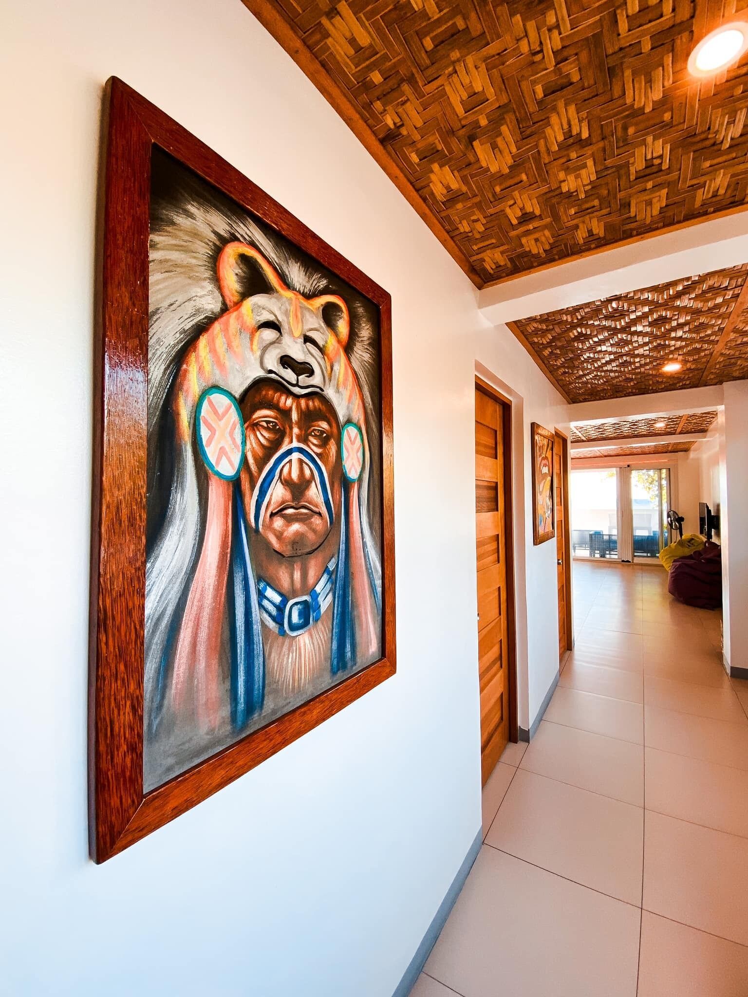 A hallway with a large painting of a bear on the wall, wooden ceiling, and a view into another room.