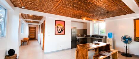 A modern kitchen with a wooden ceiling, a dining area with a wooden table and benches, and a large window providing natural light.