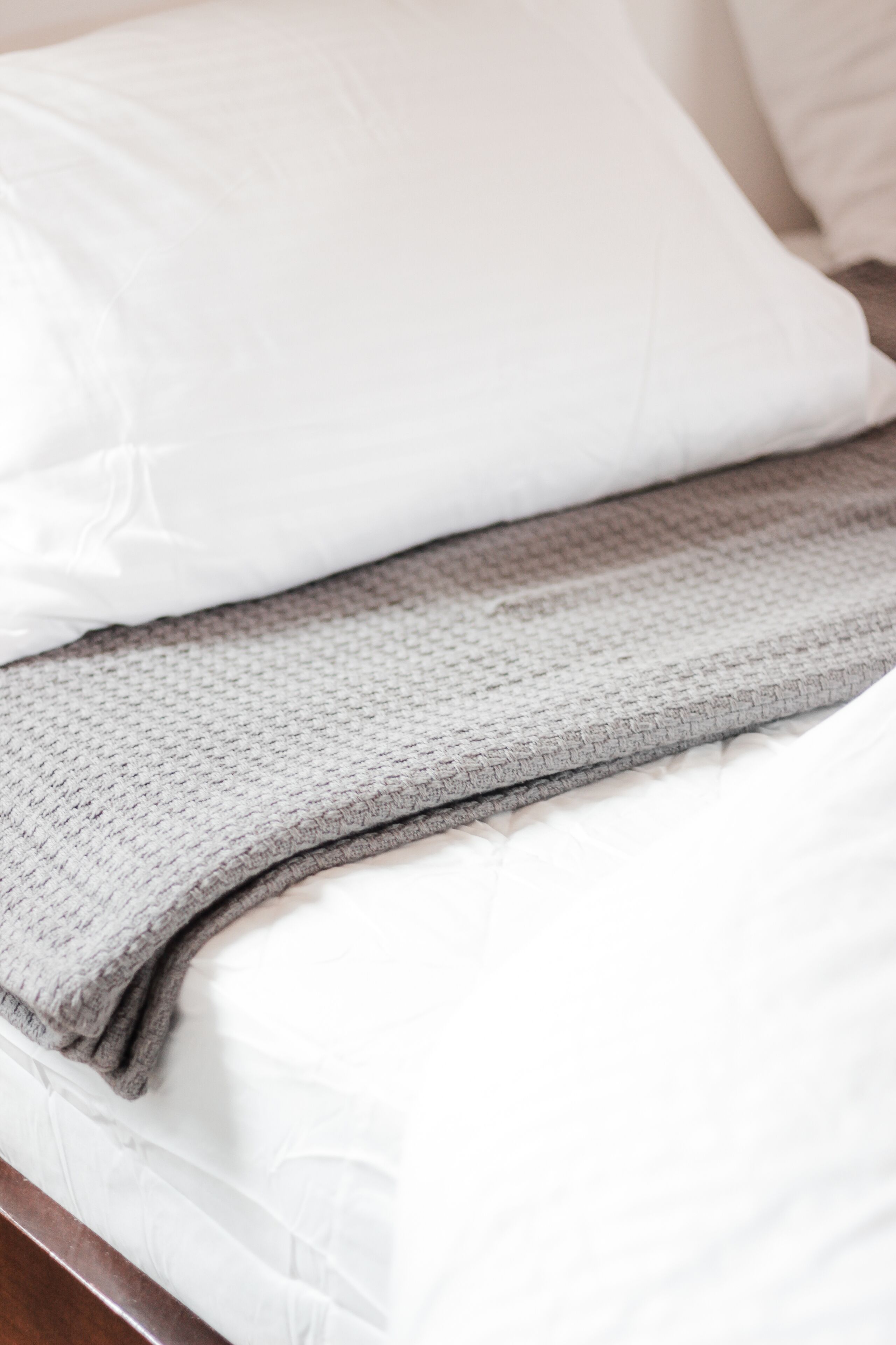 A bed with white sheets and a gray blanket.
