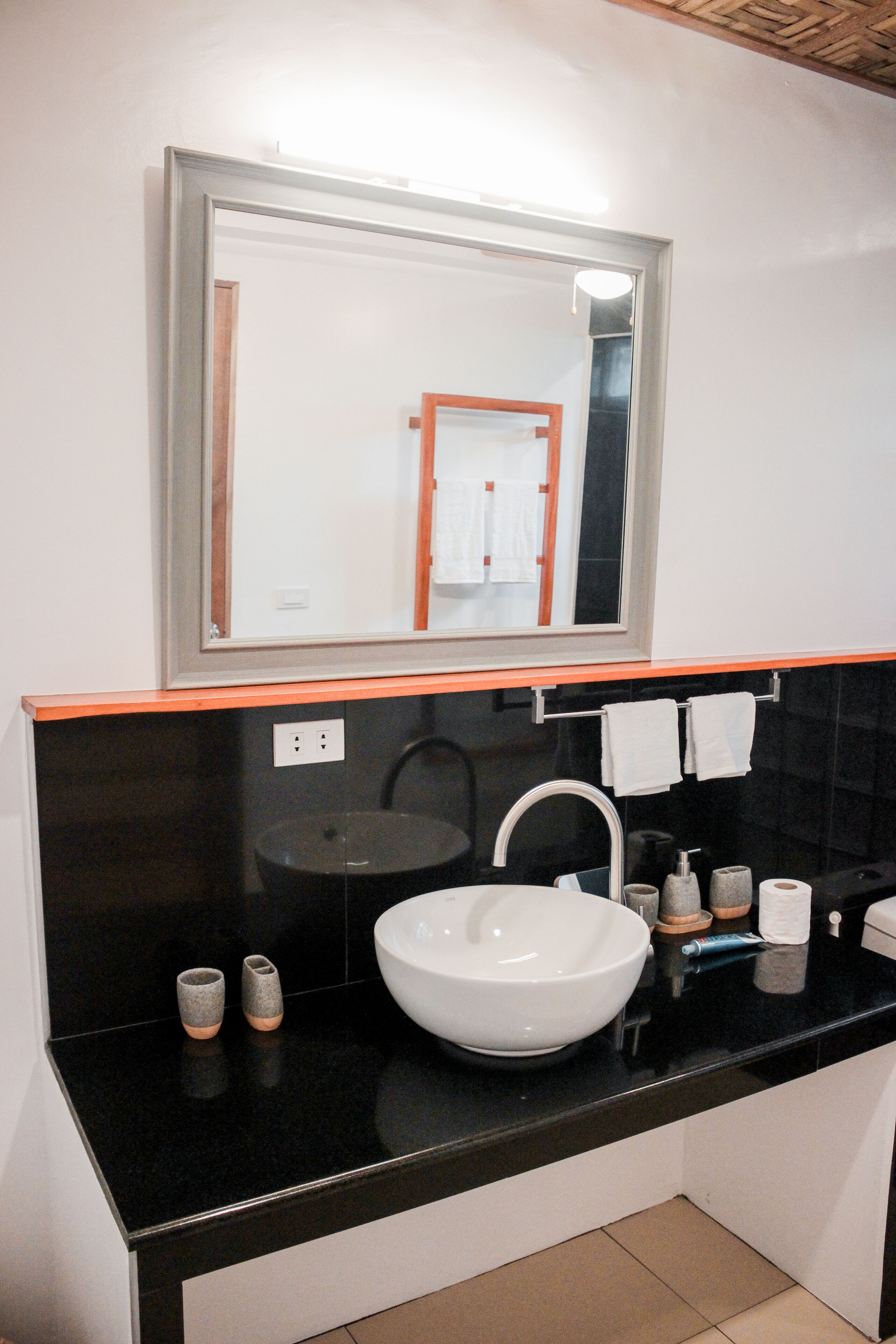A modern bathroom with a black countertop, white sink, and a large mirror above the sink.