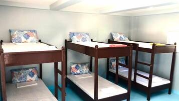 Four beds with floral-patterned pillows line a light blue wall in this simple, functional room.