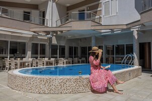 Area piscina con vasca piastrellata, mobili da esterno e una zona coperta.