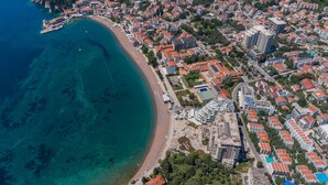 Vista aérea de un pueblo costero con playa, edificios residenciales y un puerto deportivo.