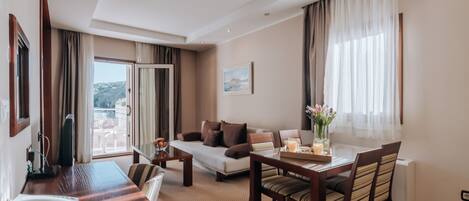 A hotel room with a dining area, a sofa, a TV, and a window with curtains.