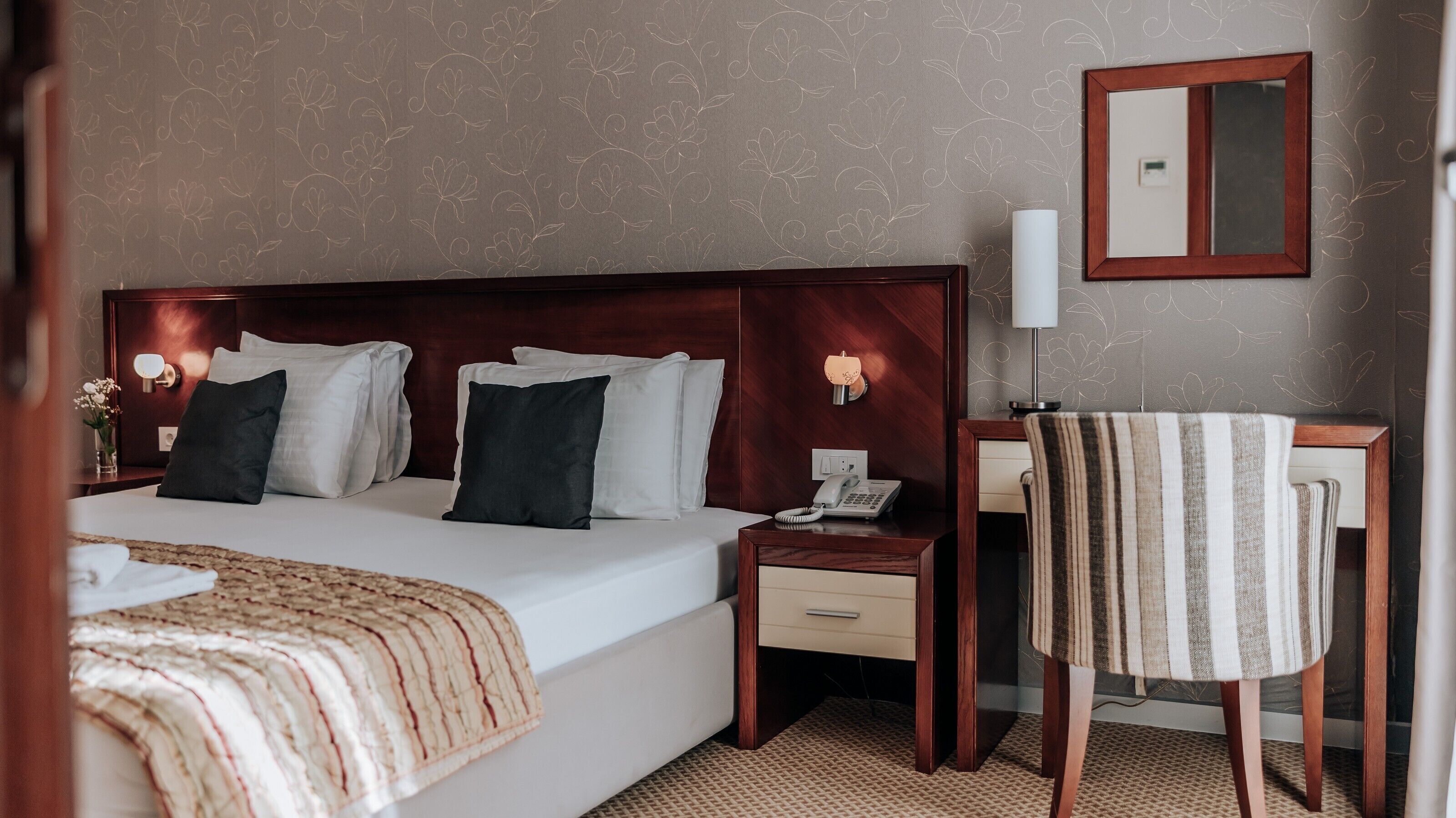 Een hotelkamer met een groot bed, bedlampen, een bureau met een telefoon en een stoel.