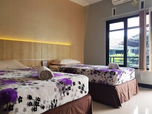 A hotel room with two beds, a wooden headboard, a window with a view of greenery, and a wall-mounted air conditioning unit. - La Derra Hotel (Purwakarta)