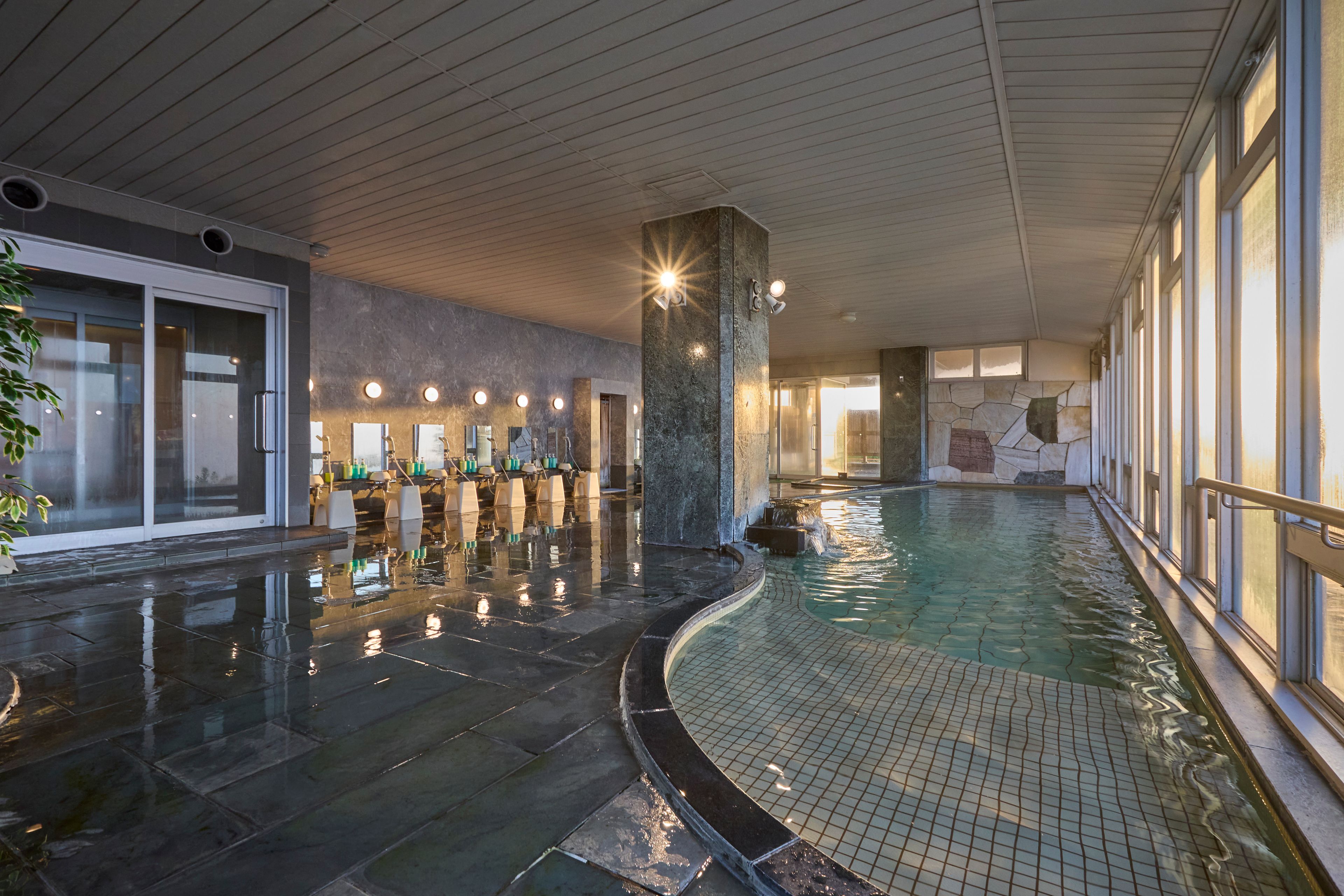 Una piscina interior con suelo de baldosas, pared de piedra y techo de madera.