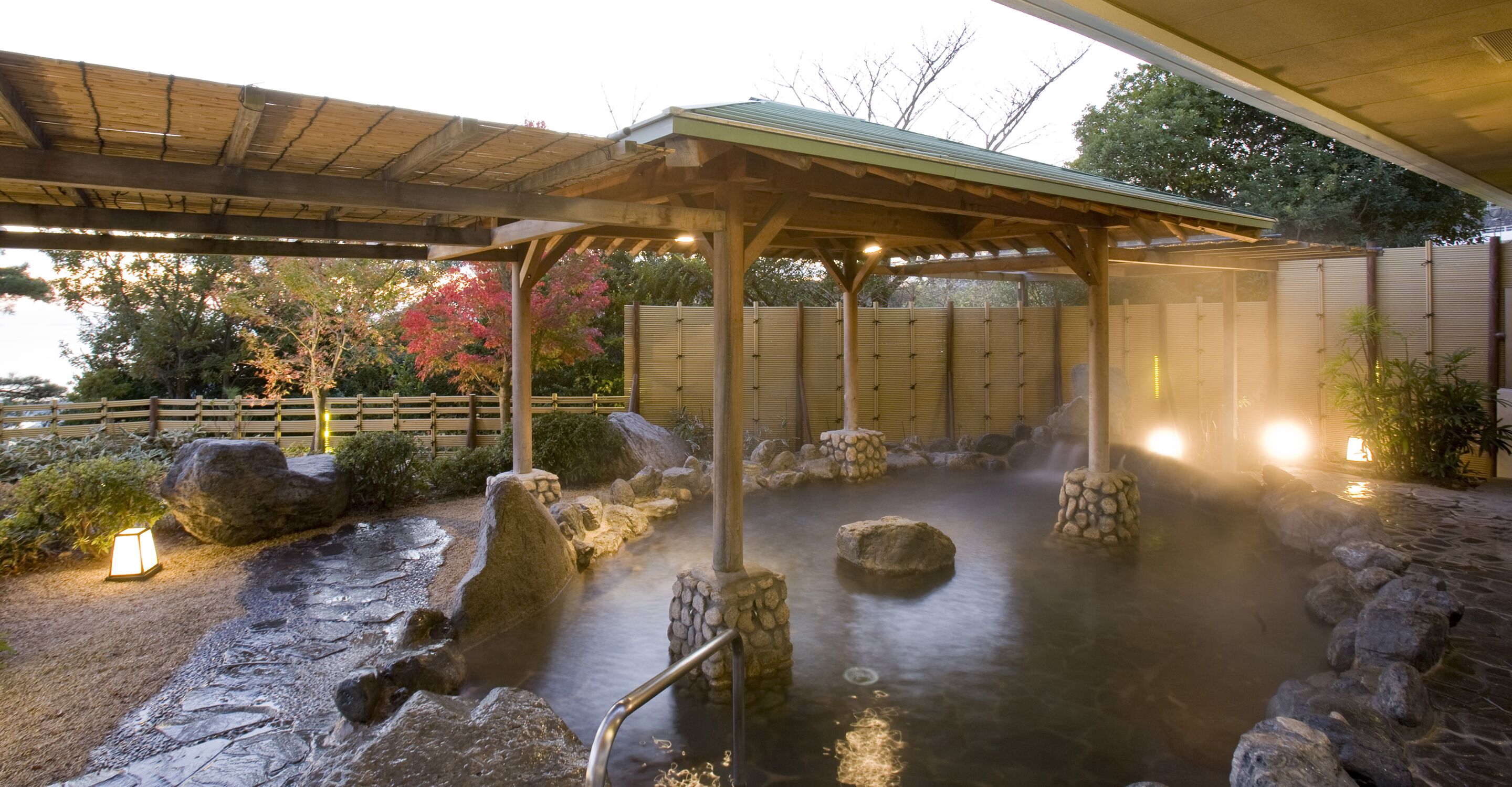 A hot spring area with stone steps leading into the water, wooden structures, and a covered seating area.