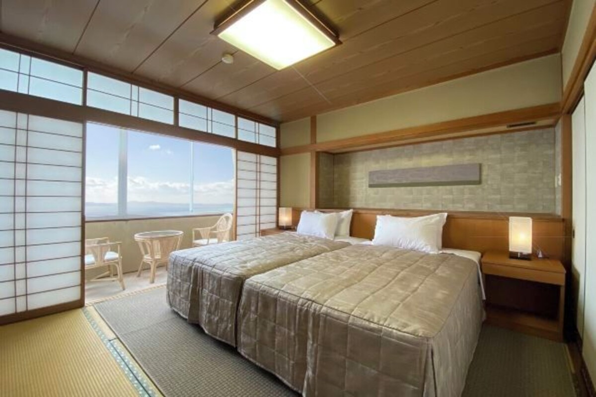 A hotel room with two beds, a view of the sky, a small table, and a chair.