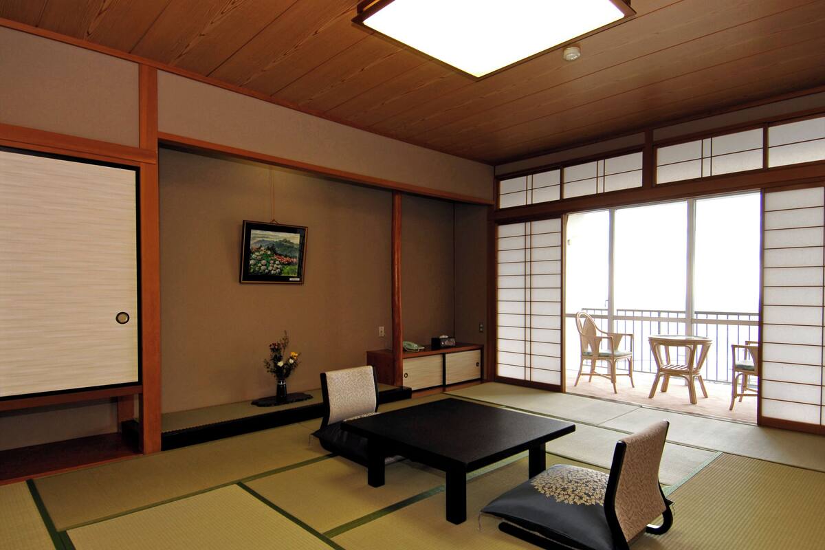 Um quarto japonês tradicional com tatames, uma mesa baixa, cadeiras e portas deslizantes.