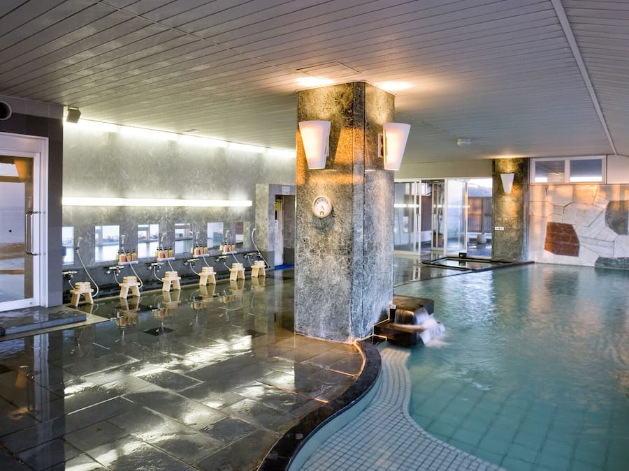 Una piscina interna moderna con un pilastro in pietra, diverse cabine spogliatoio e una parete in vetro.