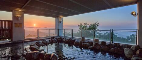 An indoor pool with a view of the sunset, surrounded by rocks and a glass barrier.