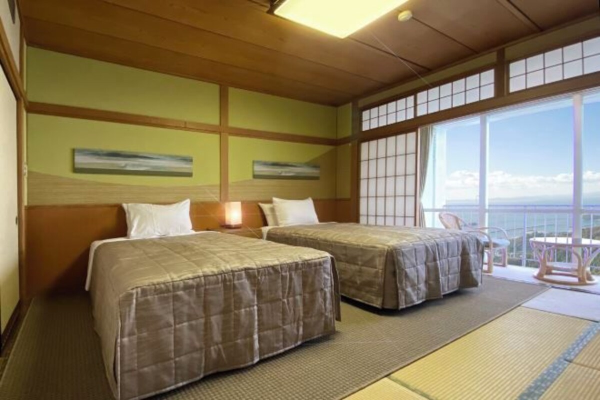A hotel room with two beds, a large window with a view, tatami mats, and a wooden ceiling.