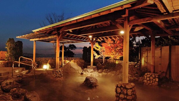 Un espacio al aire libre con calefacción, una pérgola de madera, construcciones de piedra y vistas a árboles al fondo.